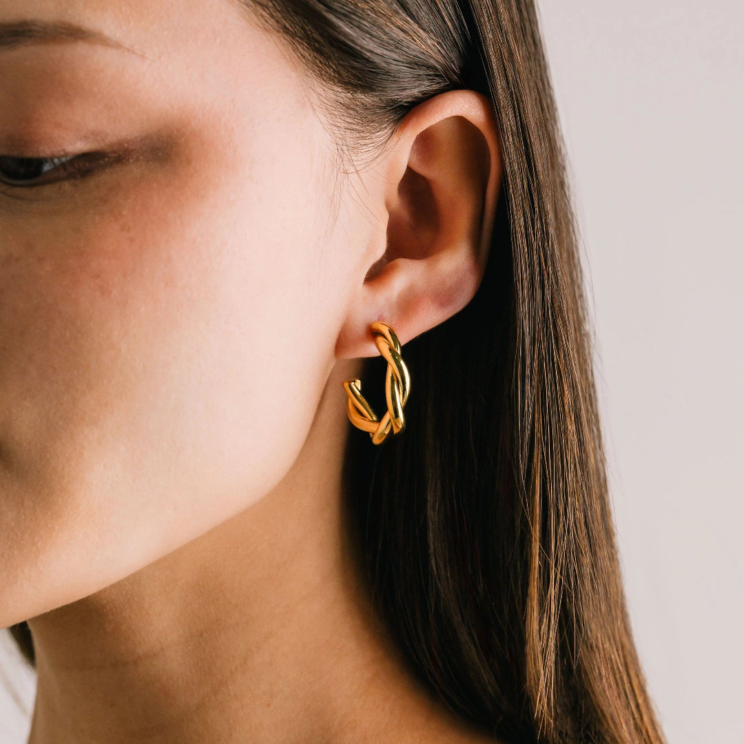 Close-up of a person wearing gold hoop earrings with a neutral background