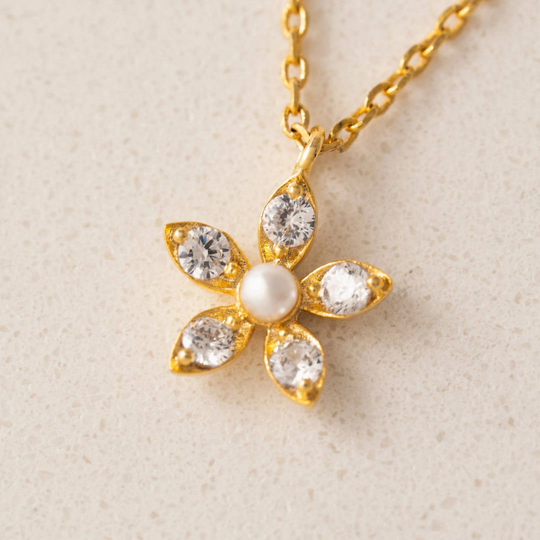 Gold flower-shaped necklace with a pearl center on a beige background