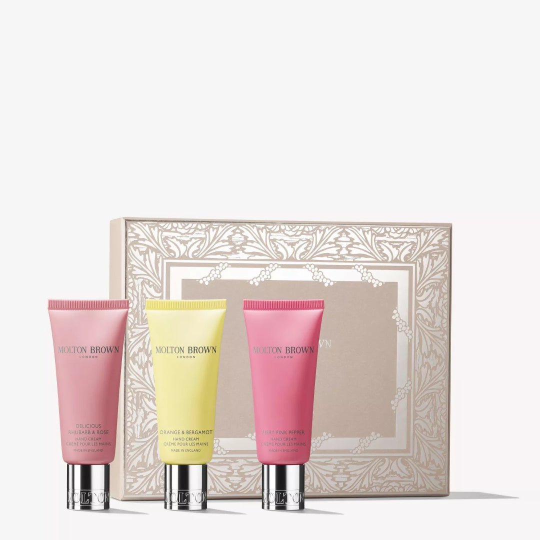 Three Molton Brown hand creams in front of a decorative box on a white background