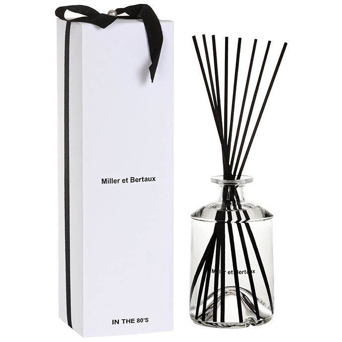 A clear glass fragrance diffuser with black tuberose, white iris, and rose notes, alongside its white packaging box with a black ribbon.