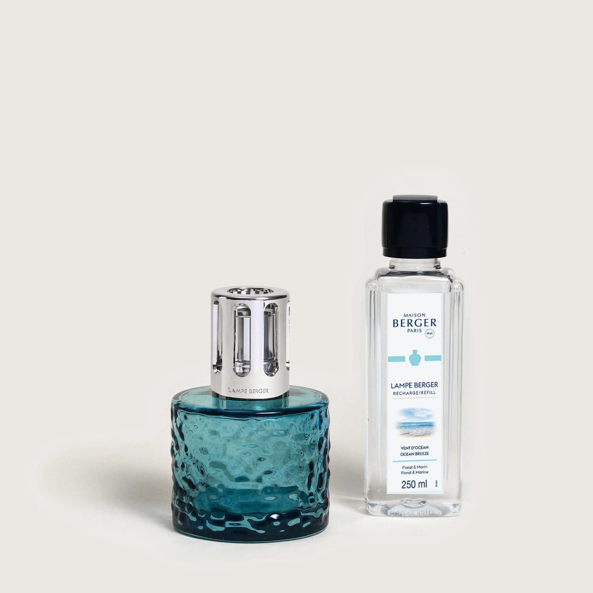 A blue Maison Berger fragrance lamp with a metallic top next to a clear bottle labeled 'BERGER' containing a white liquid.