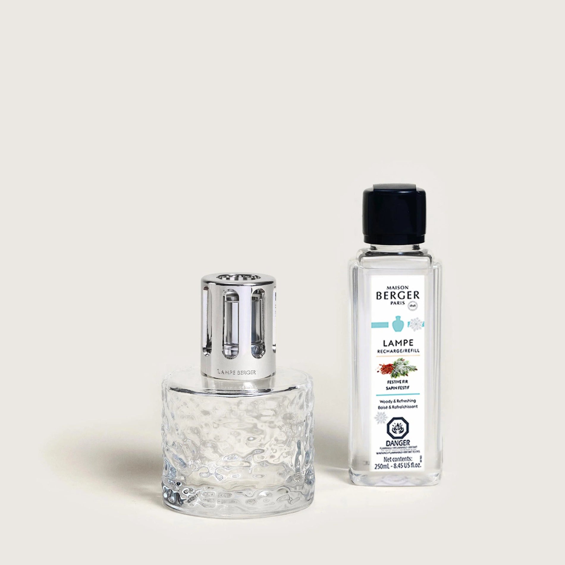 A clear fragrance lamp with a metallic top alongside a bottle of Maison Berger fragrance fuel.