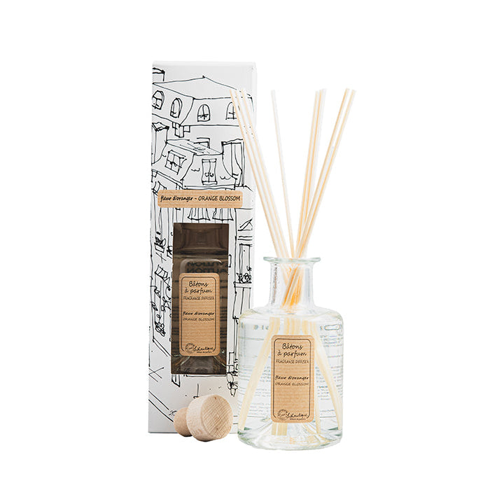 A Authentique Orange Blossom Fragrance Diffuser by Lothantique, featuring a clear glass bottle with a white label, several reeds inside, and a decorative item on the side.