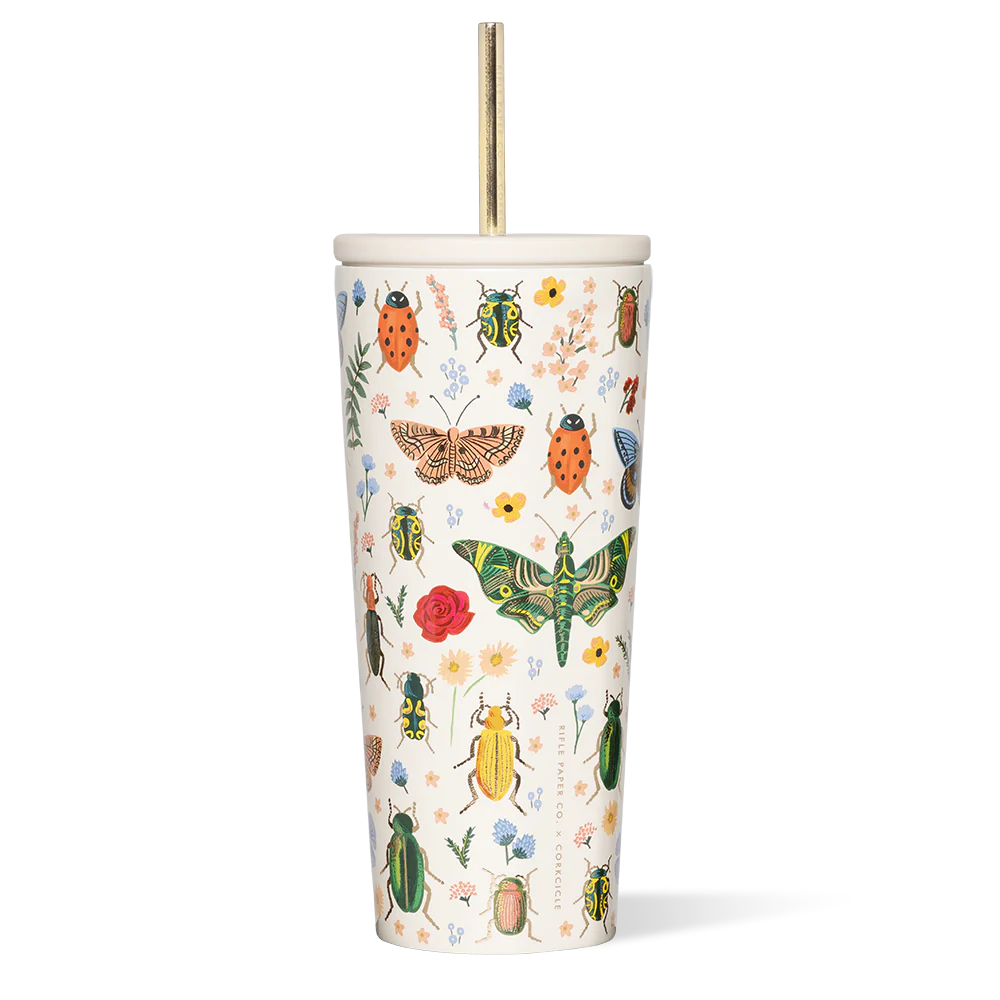 A tall white reusable straw cup with Rifle Paper Co's floral print, featuring various insects and flowers, paired with a gold-colored metal straw.