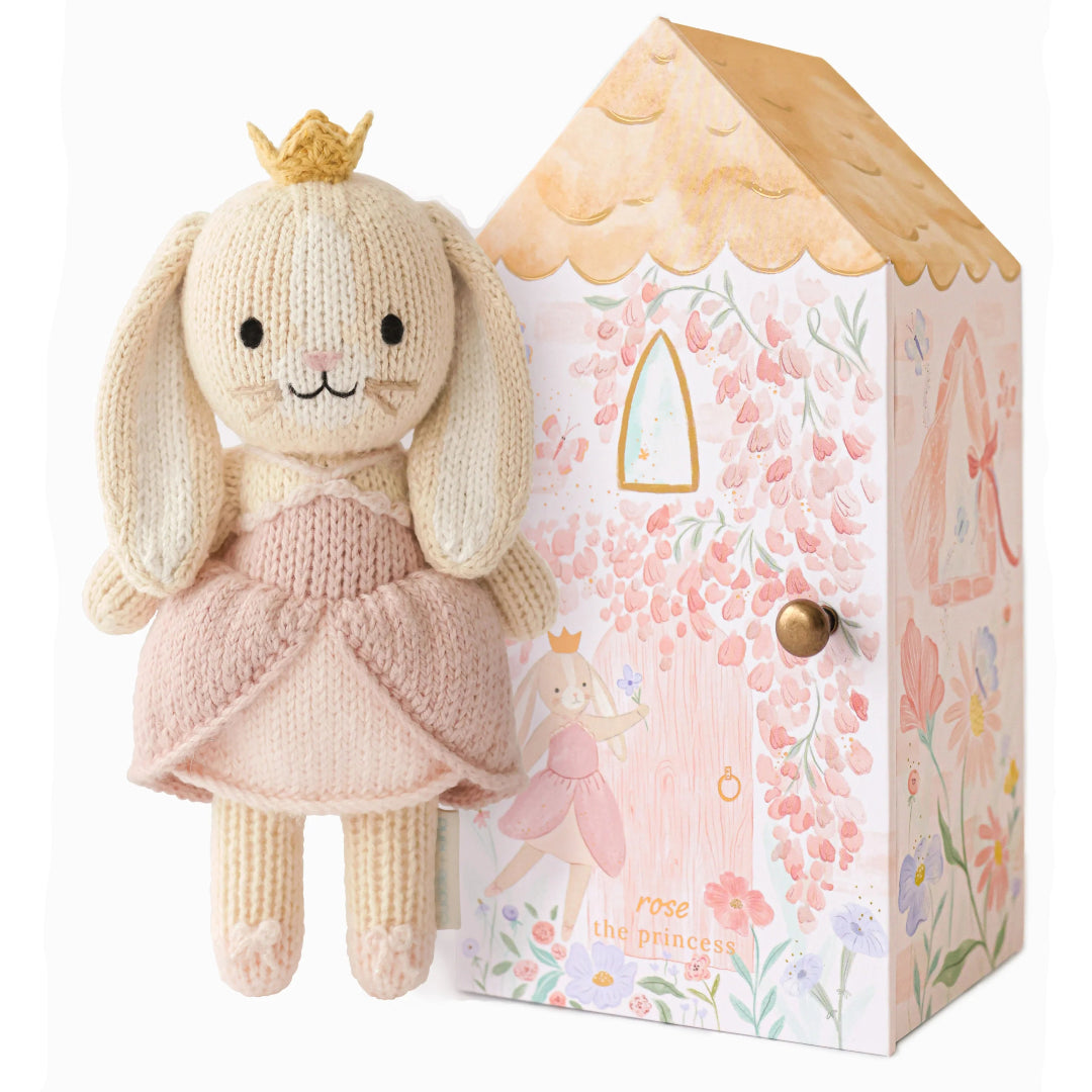 Knitted bunny toy with a pink dress and gold crown next to a decorative box with fairy design.