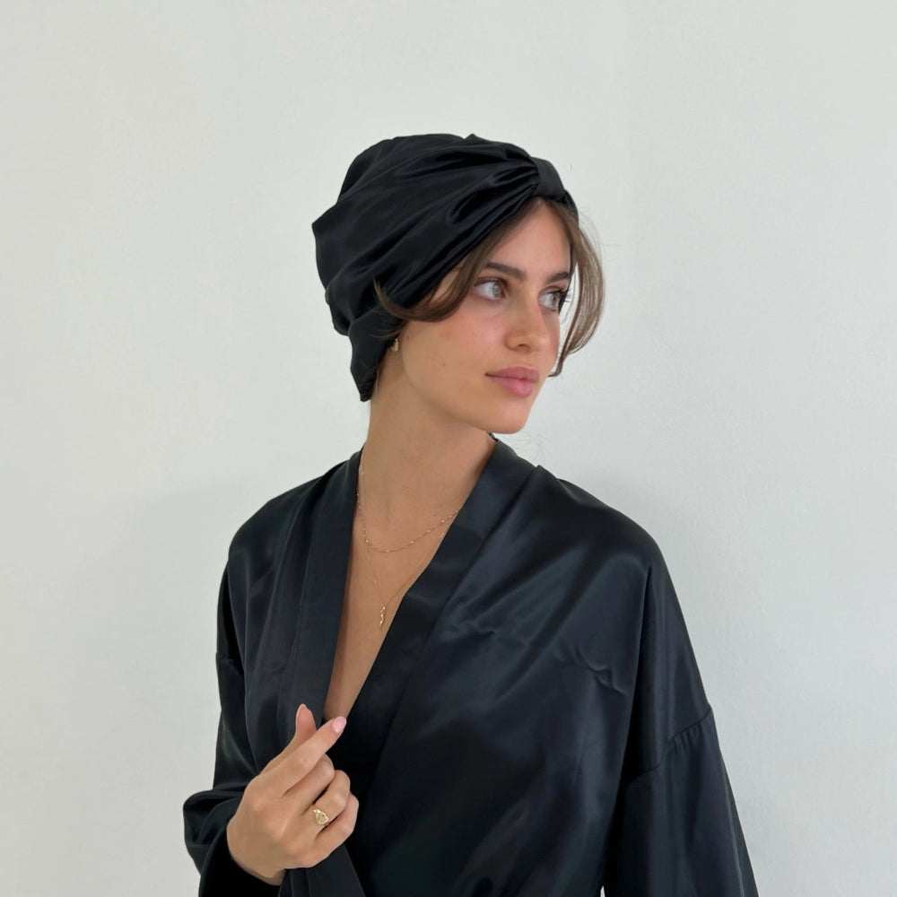 Woman wearing a black headscarf and black outfit against a plain background