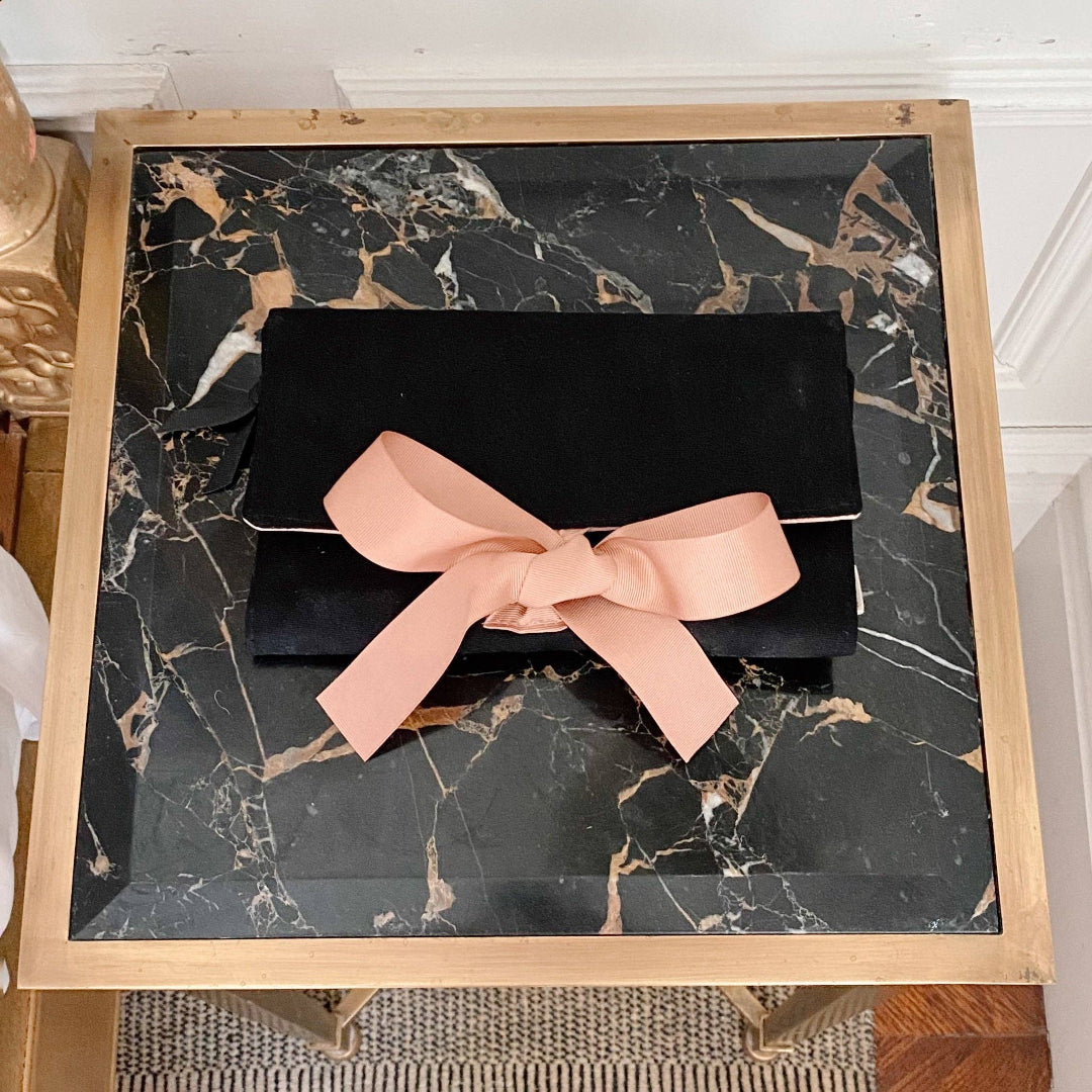 Black clutch with a pink bow on a marble table