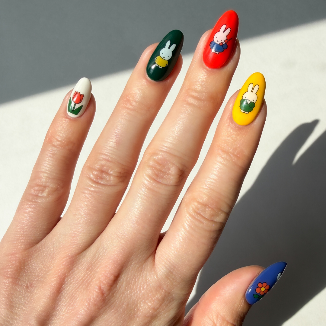 Hand with colorful nail art featuring Miffy characters on a neutral background