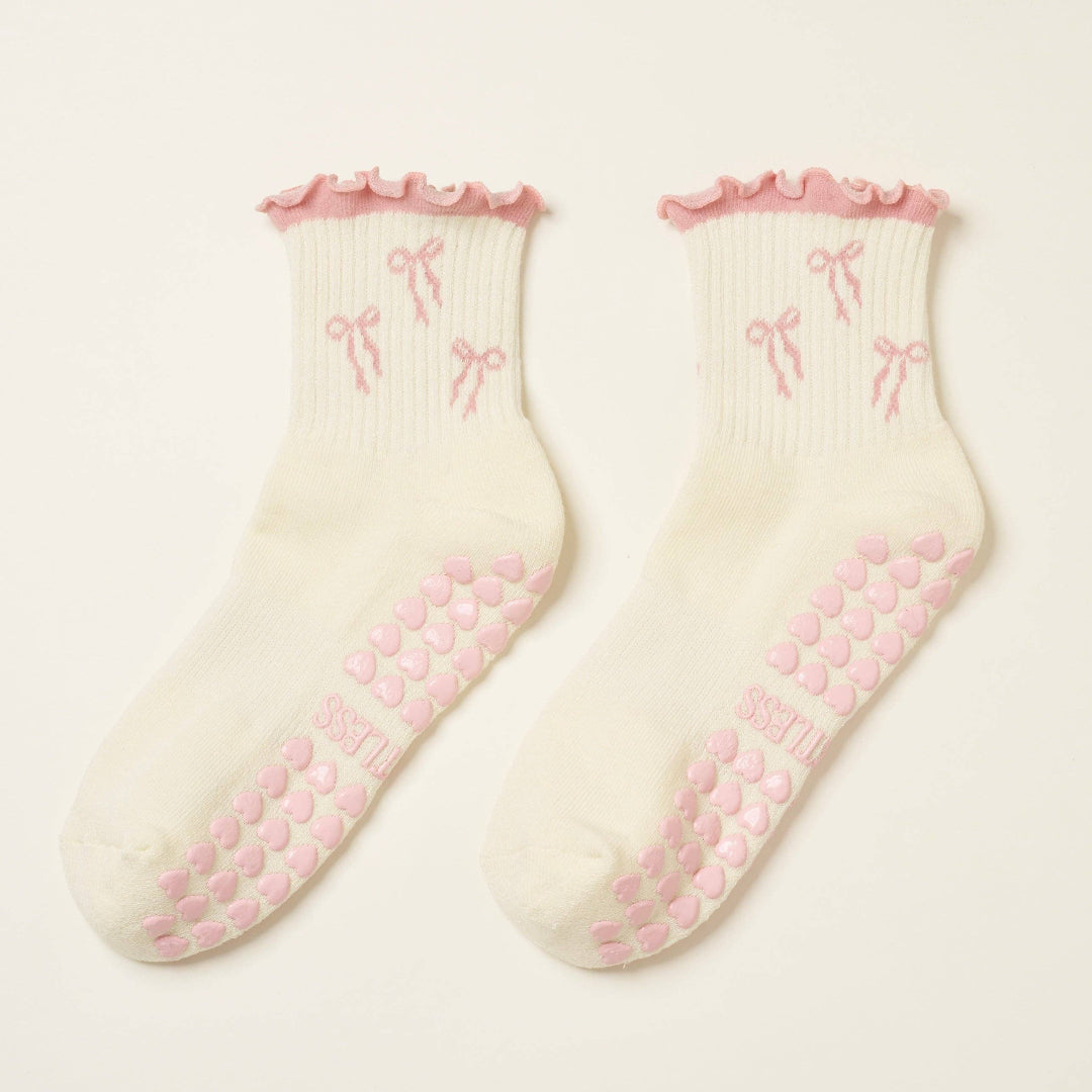 Pair of cream socks with pink bows and textured sole on a light pink background