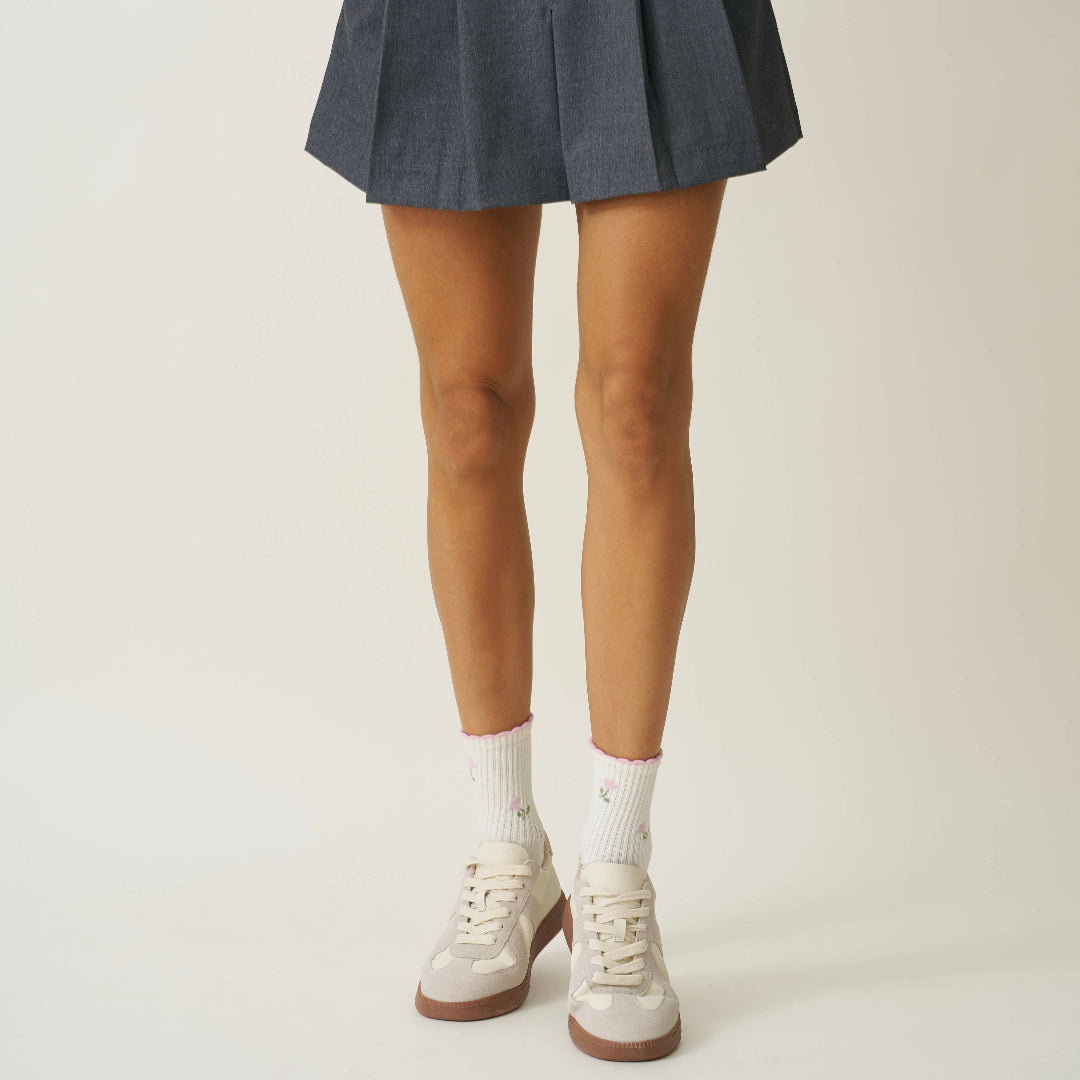 Person wearing a pleated skirt with white shoes and socks on a plain background
