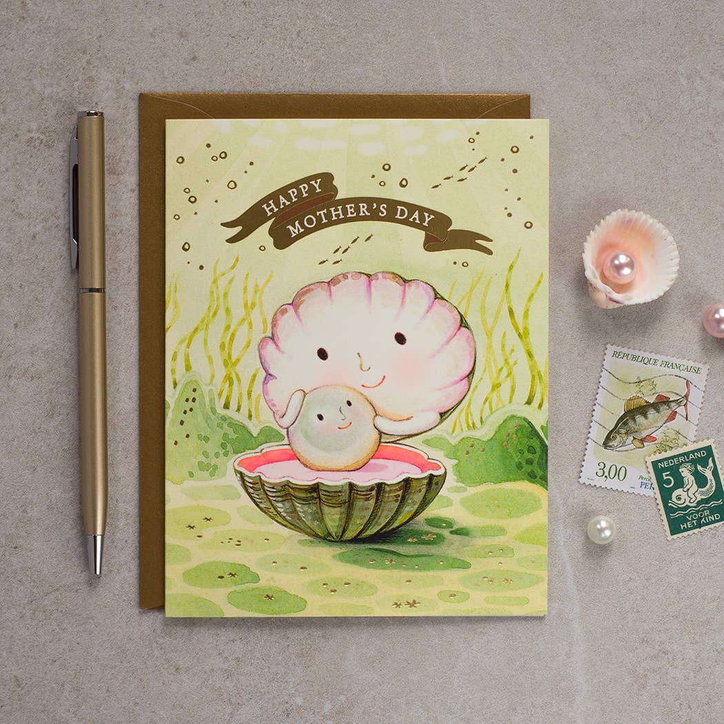 Mother's Day card with a shell and baby illustration, pen, and stamps on a gray surface