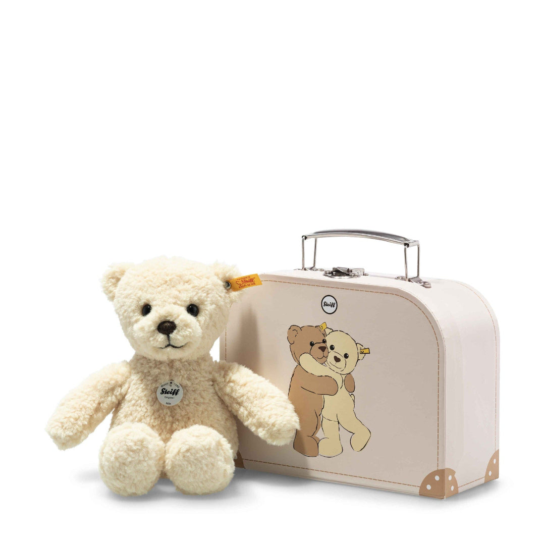 A vanilla-yellow teddy bear next to a pink suitcase with a graphic of two bears hugging on the side.