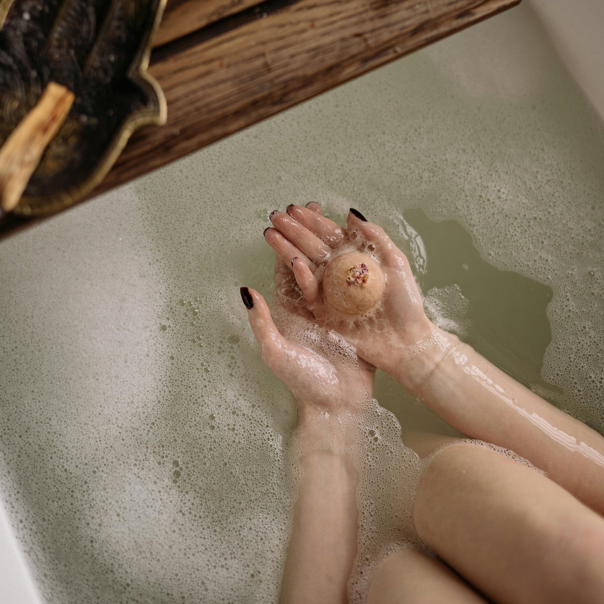 Person holding a loofah in a bathtub with a wooden shelf above