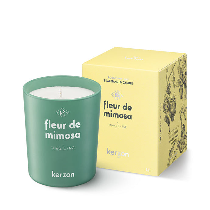 A green Kerzon Fleur de Mimosa fragranced candle with its yellow packaging box. The candle is labelled with the brand and product name, and has a braided green wick.