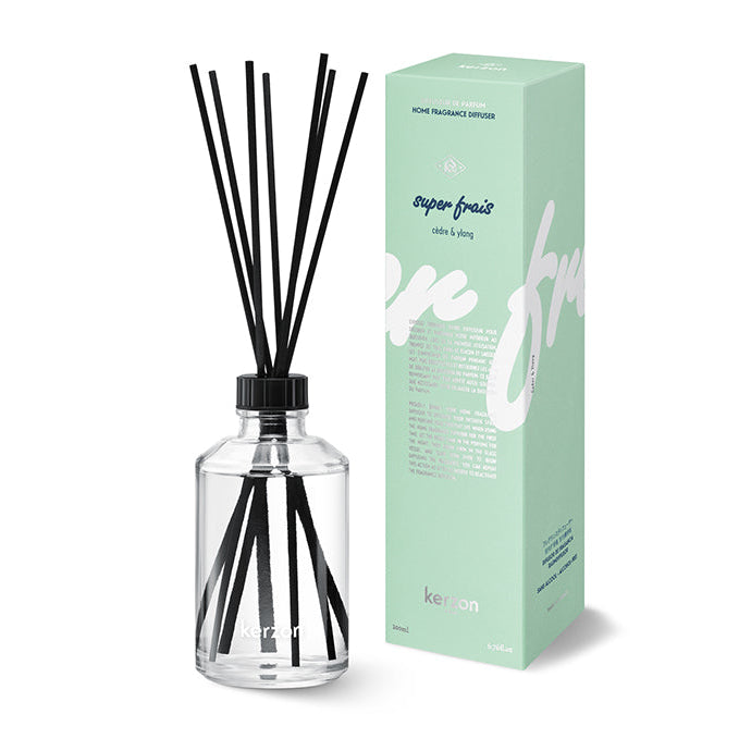 A clear glass fragrance diffuser with black sticks, alongside its green packaging box with product information.