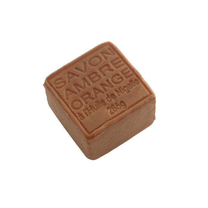 A brown cube-shaped soap with 'SAVON AMBRE ORANGE' embossed on it, indicating it is an amber-orange scented soap from Atelier du Savon.